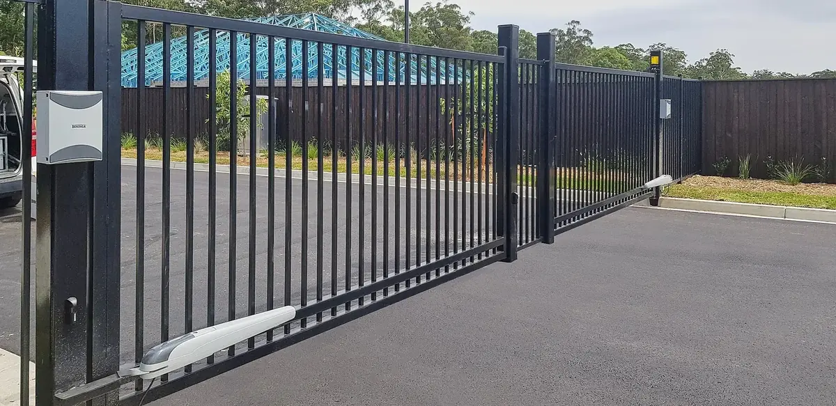 Black automated sliding driveway gate with a ground track and motor at a residential property.